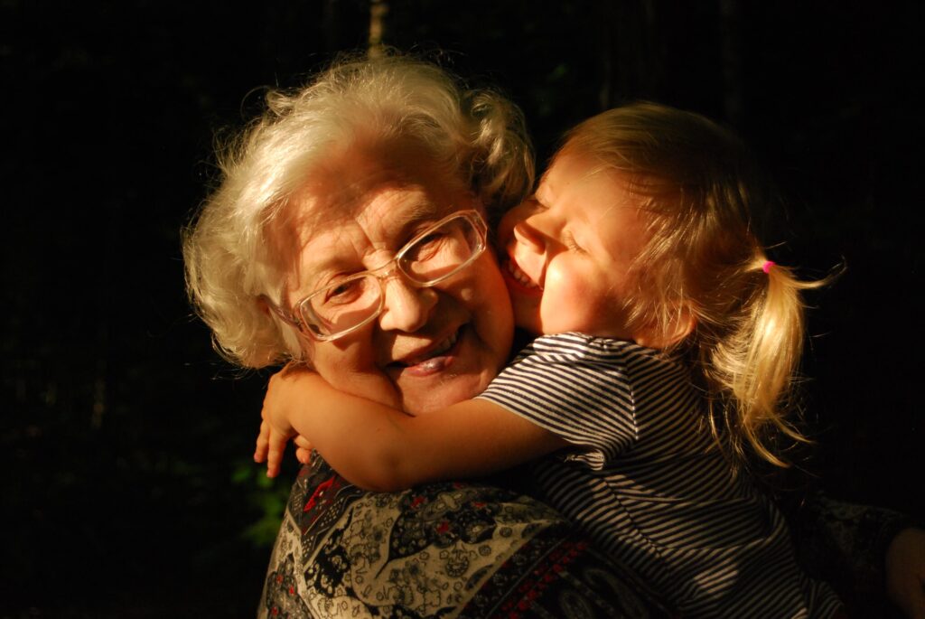An older woman smiling which a young kid kisses them
